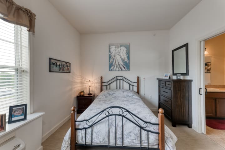 A cozy bedroom with a metal-framed single bed, decorated with artwork and a wooden dresser.