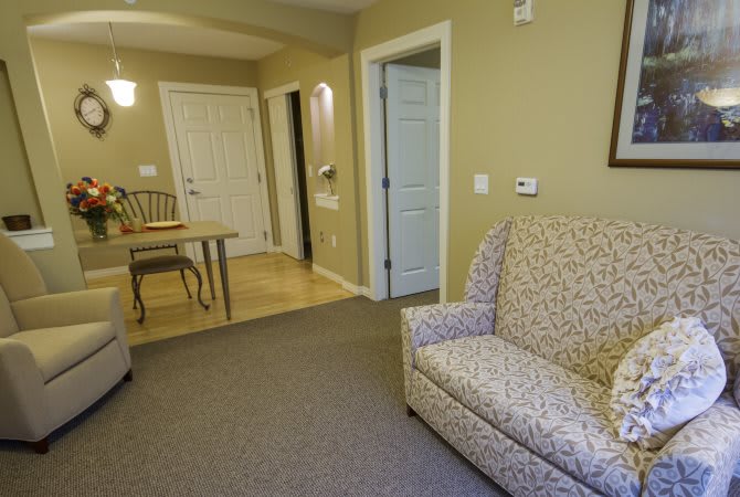 A cozy living room with a patterned armchair, small dining table, and neutral tones.