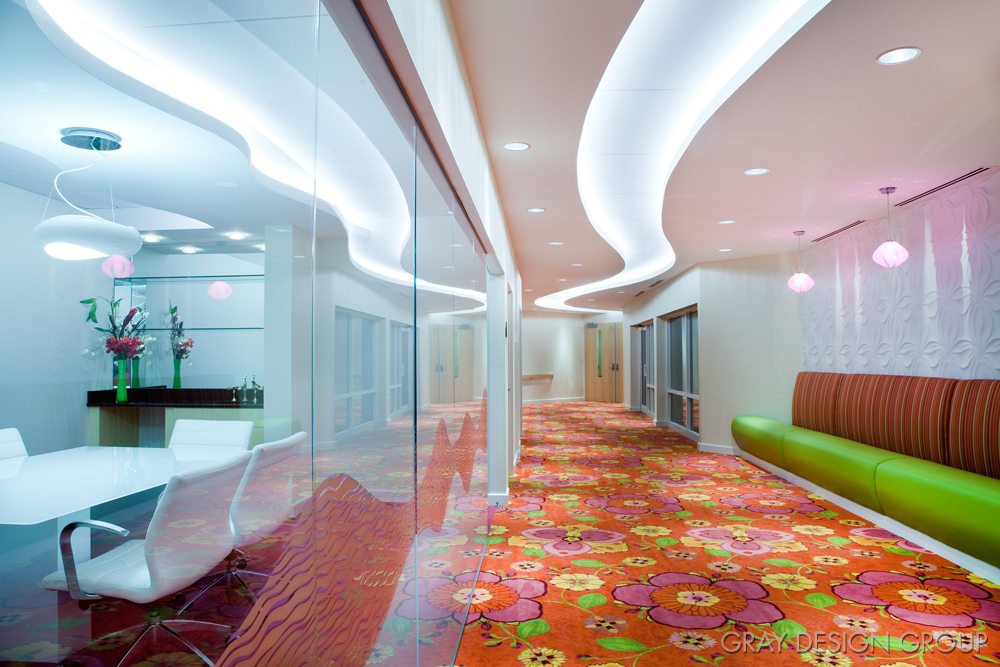 A modern office hallway featuring vibrant carpet patterns and sleek glass walls.