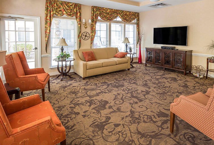 A spacious living room featuring a sofa, ornate patterned carpet, and a large television.