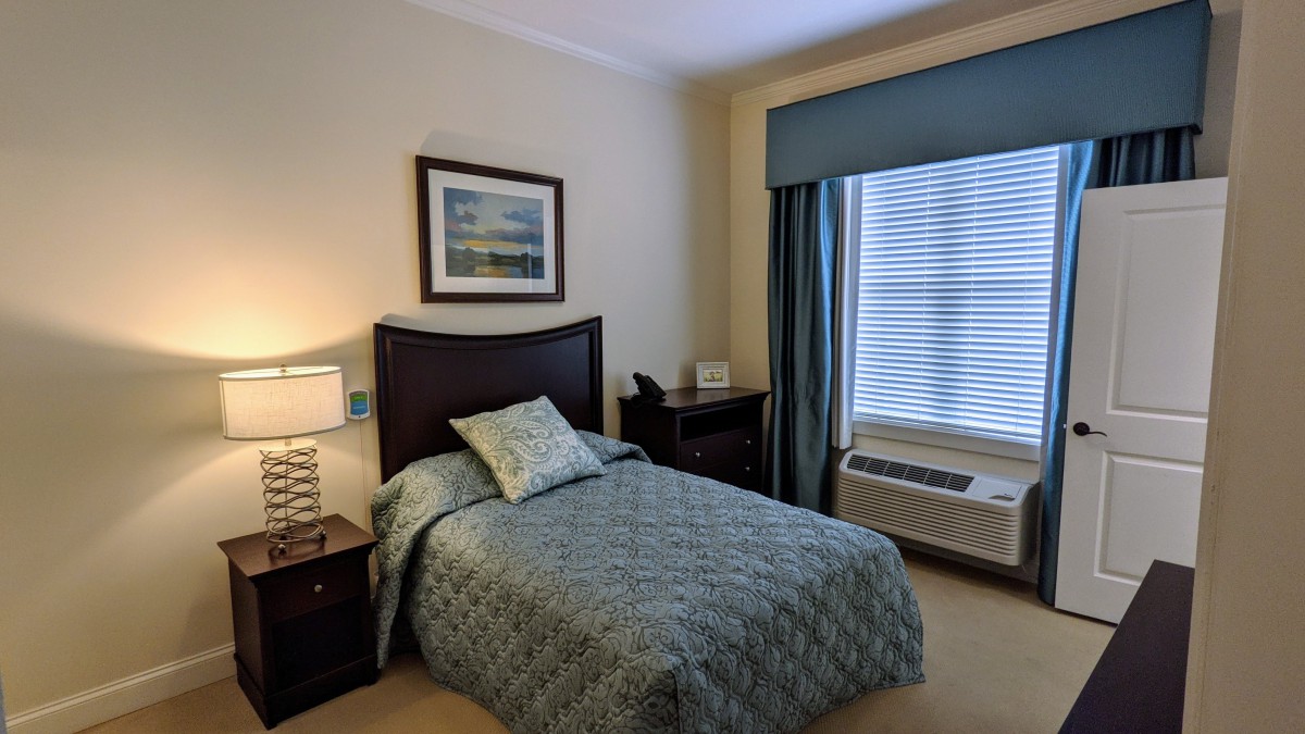 A neatly arranged bedroom with a single bed, nightstand, and large window with curtains.