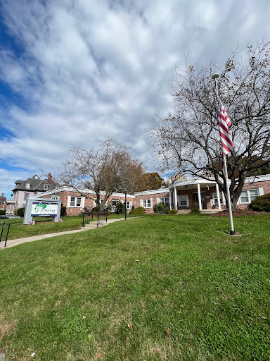 A peaceful scene featuring a building with an American flag in front, surrounded by green grass and a partly cloudy sky.