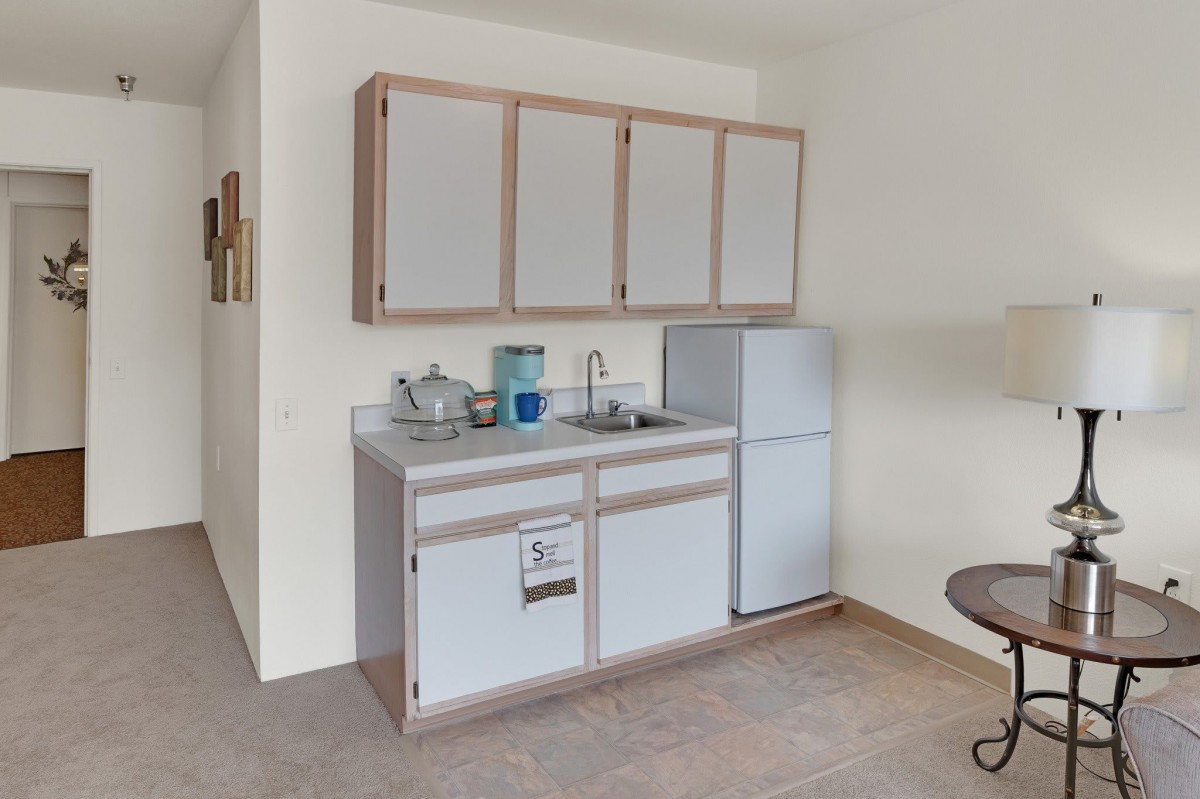 A compact kitchen setup featuring a small sink, upper and lower cabinets, and a refrigerator in an apartment.