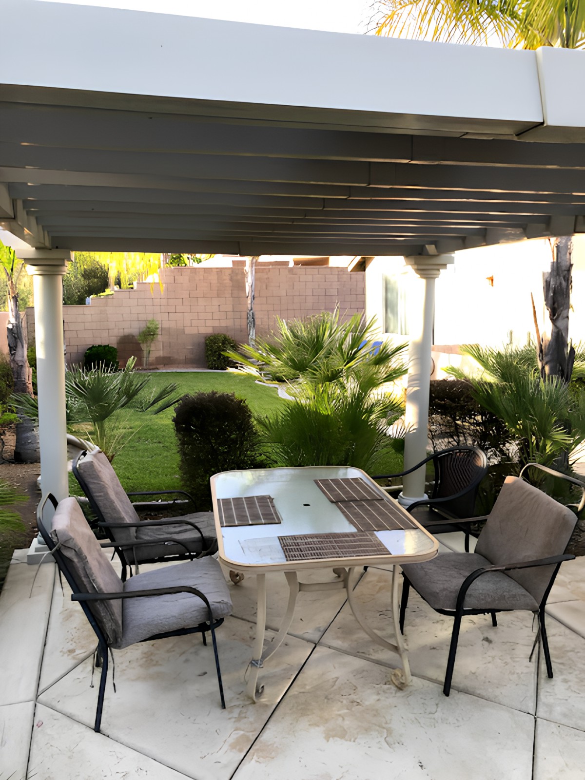 A cozy patio with a table and chairs set under a covered area, surrounded by lush greenery in the backyard.