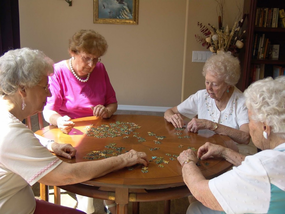 A group of elderly women engaged in assembling a puzzle at a table.