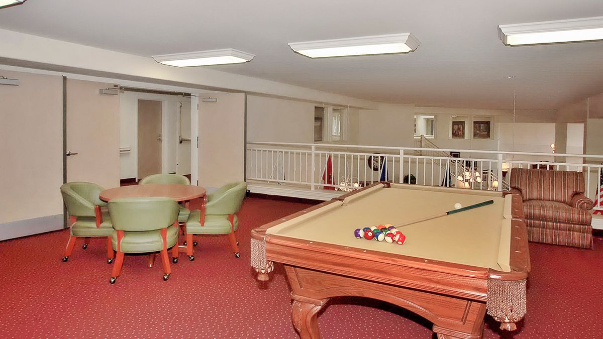 A cozy game room featuring a billiards table and a seating area with chairs on red carpet.