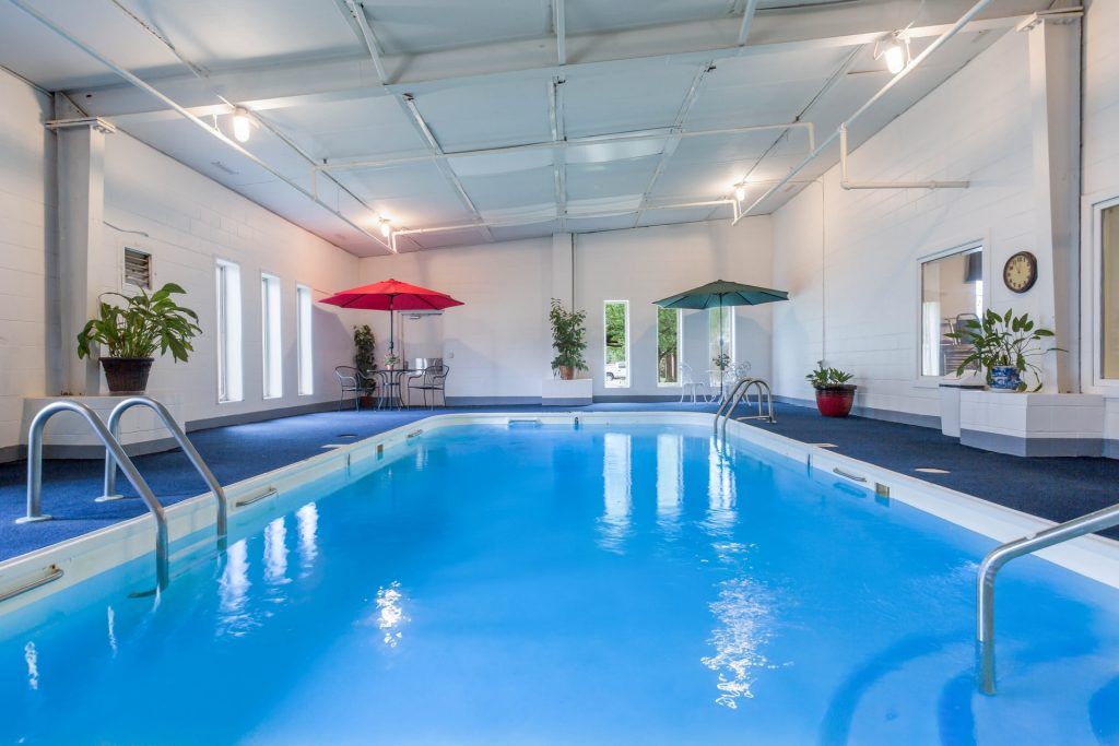 A serene indoor swimming pool area with umbrellas and potted plants.