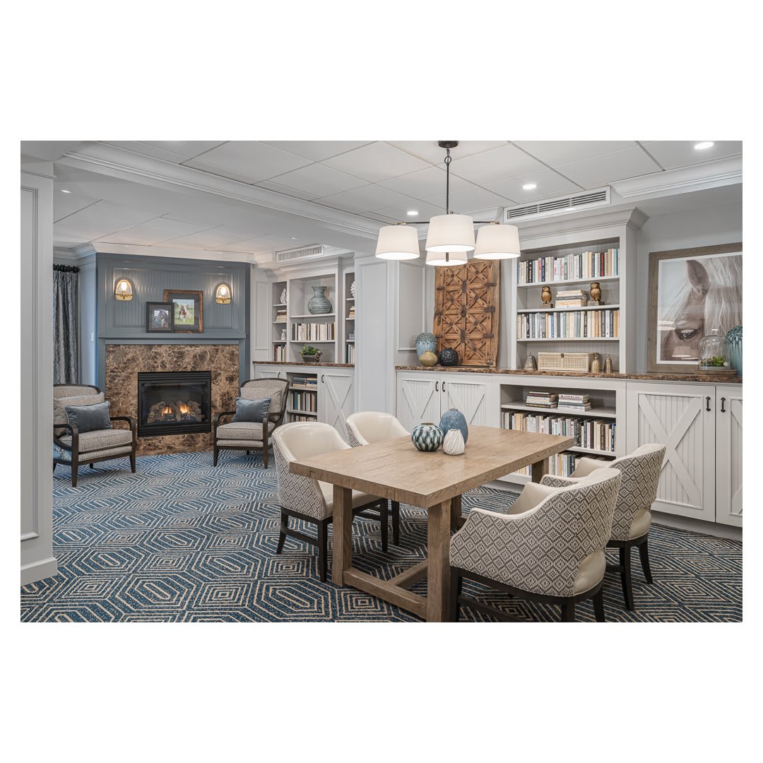 A modern living and dining area featuring a cozy fireplace, elegant furniture, and neatly organized bookshelves.