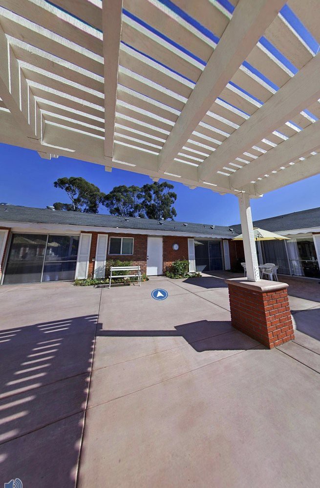 A sunny courtyard with a pergola and brick pillar providing shade.