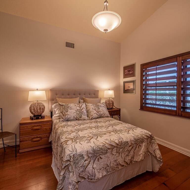 A cozy bedroom with a bed, nightstands, lamps, and window shutters.
