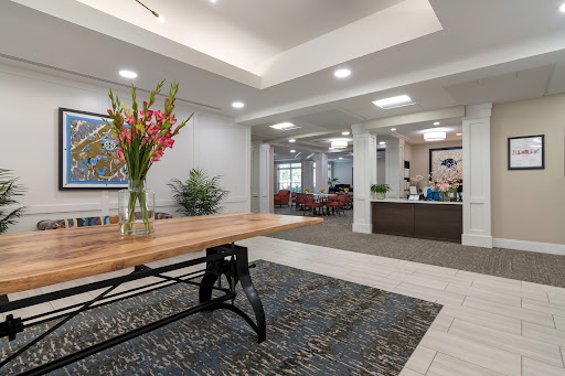 A modern lobby featuring a wooden table with floral arrangements and a reception area in the background.