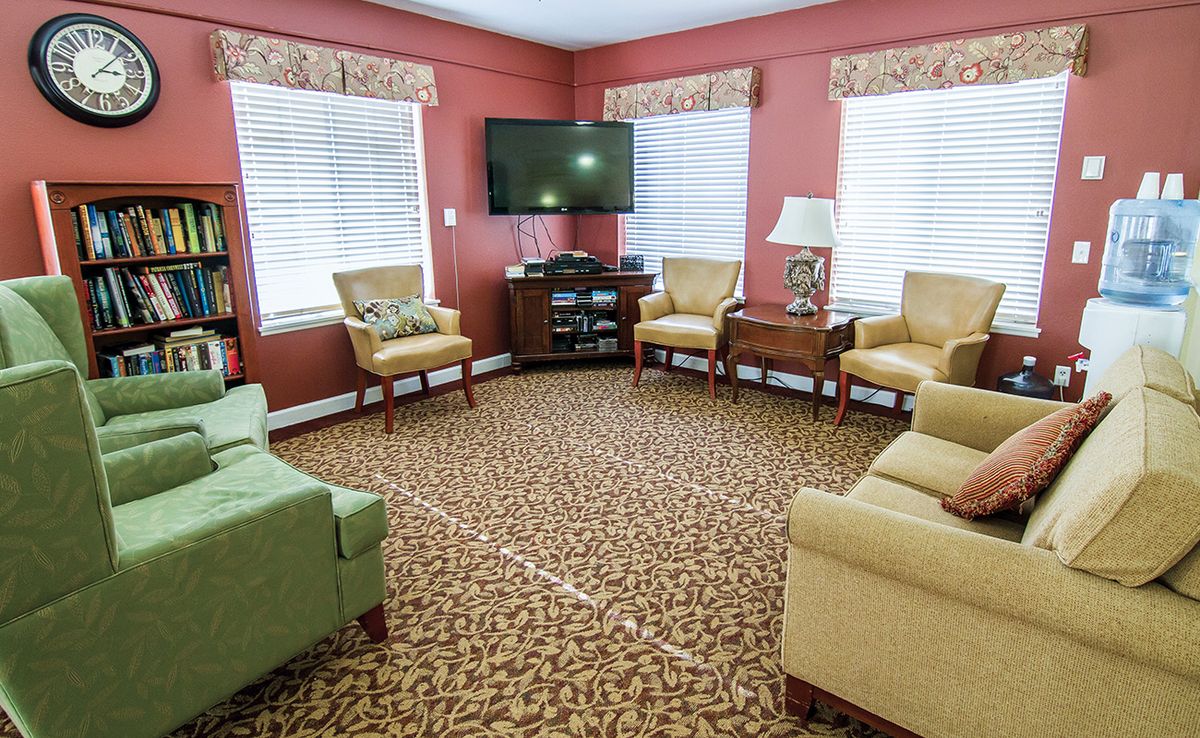 A cozy living room with sofas and armchairs arranged around a television, featuring a patterned carpet and warm color tones.