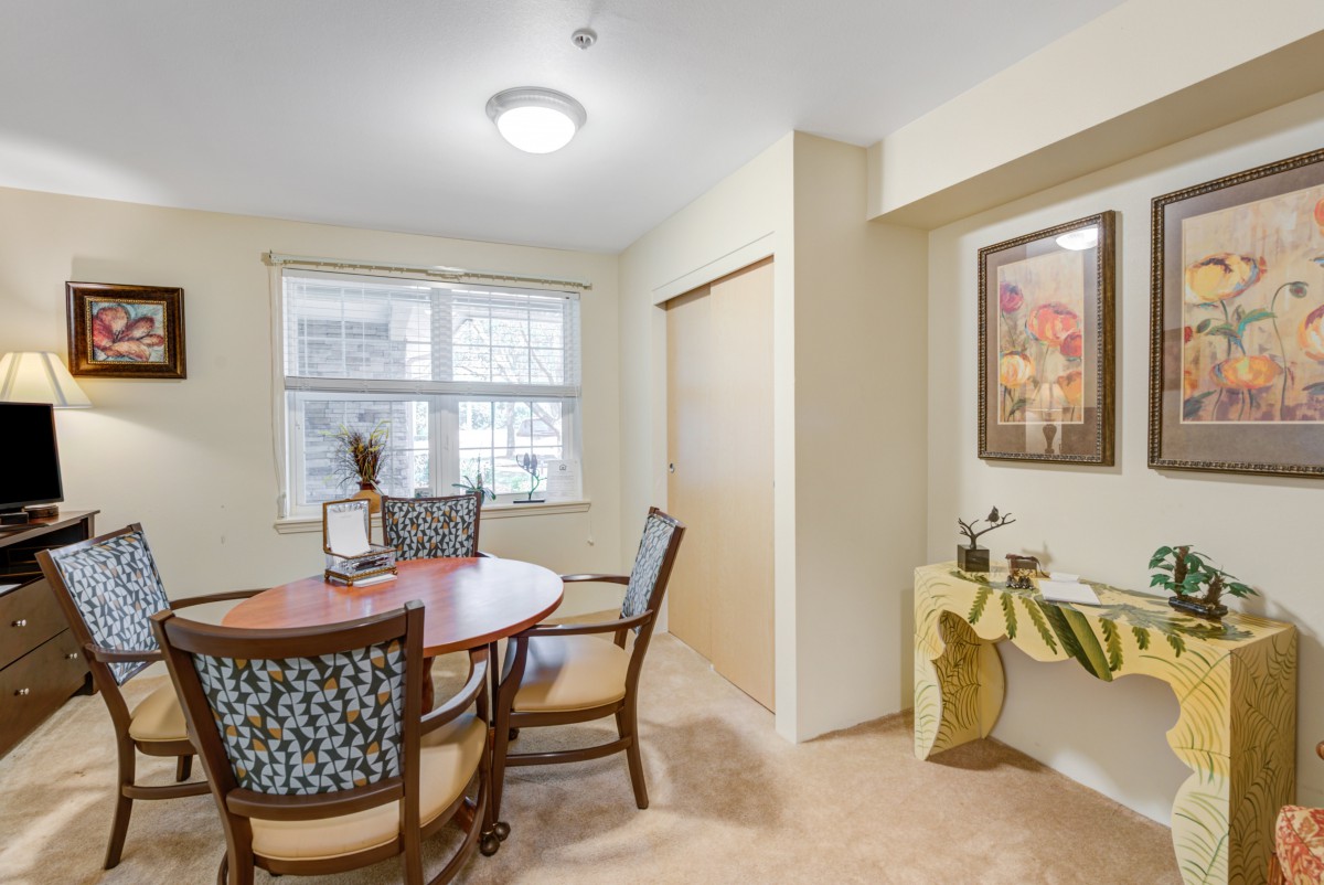 A cozy dining area with a round table and four chairs, featuring artwork on the wall and natural light from the window.