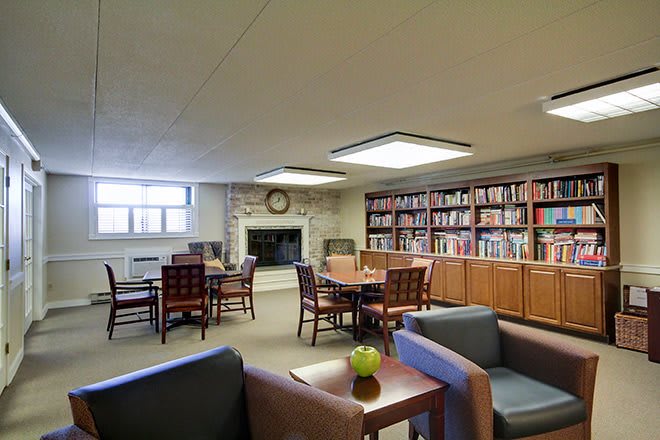 A cozy library reading room with bookshelves, tables, and a fireplace.