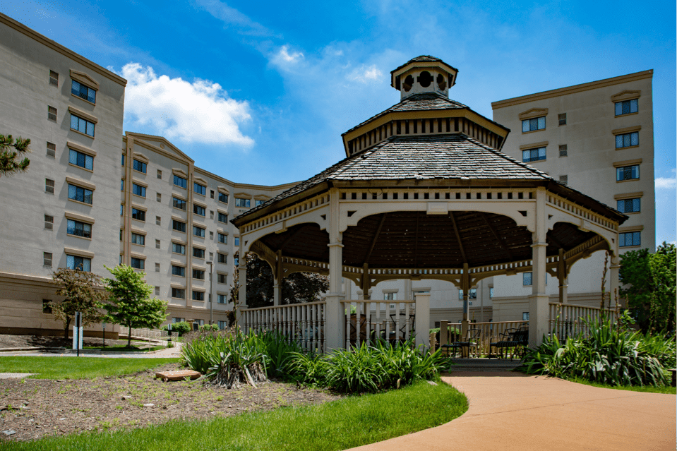 A gazebo in a landscaped garden area surrounded by a multi-story building under a bright blue sky.