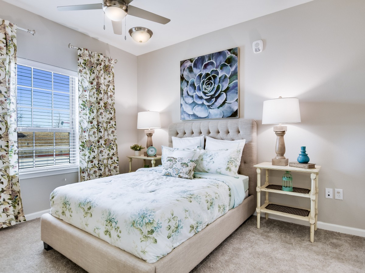 A cozy bedroom featuring a floral-themed bedspread, elegant artwork above the headboard, and stylish nightstands with lamps.