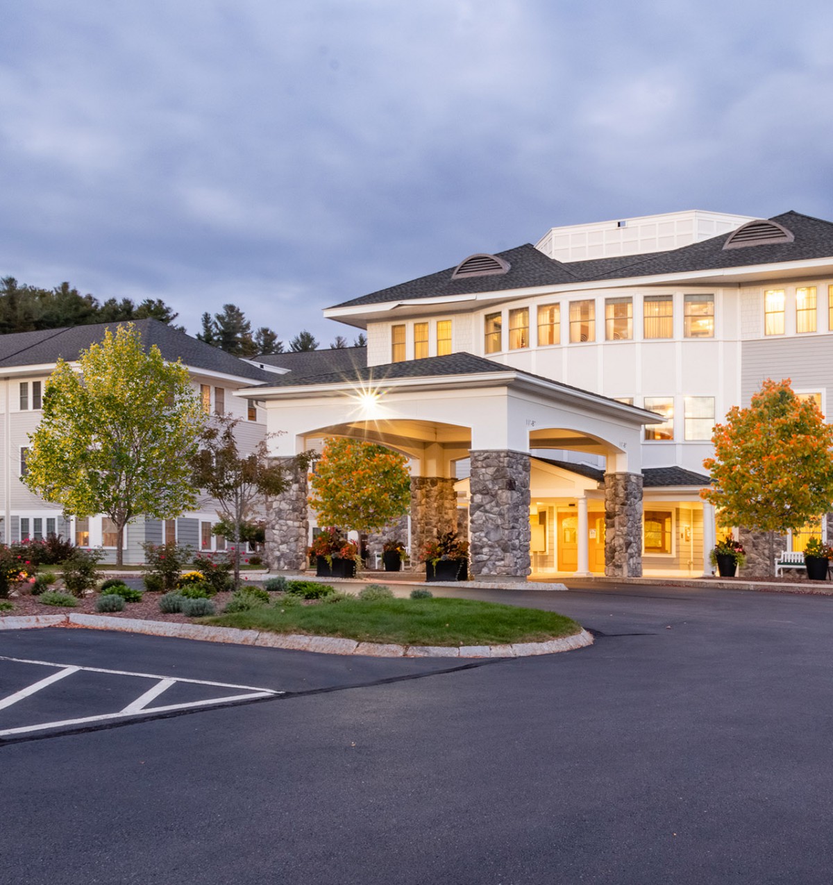 A large building with a welcoming entrance, surrounded by trees and set against an evening sky.