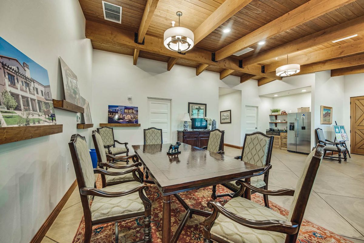 A spacious conference room featuring a large meeting table, elegant chairs, a wooden ceiling with chandeliers, and wall decor.