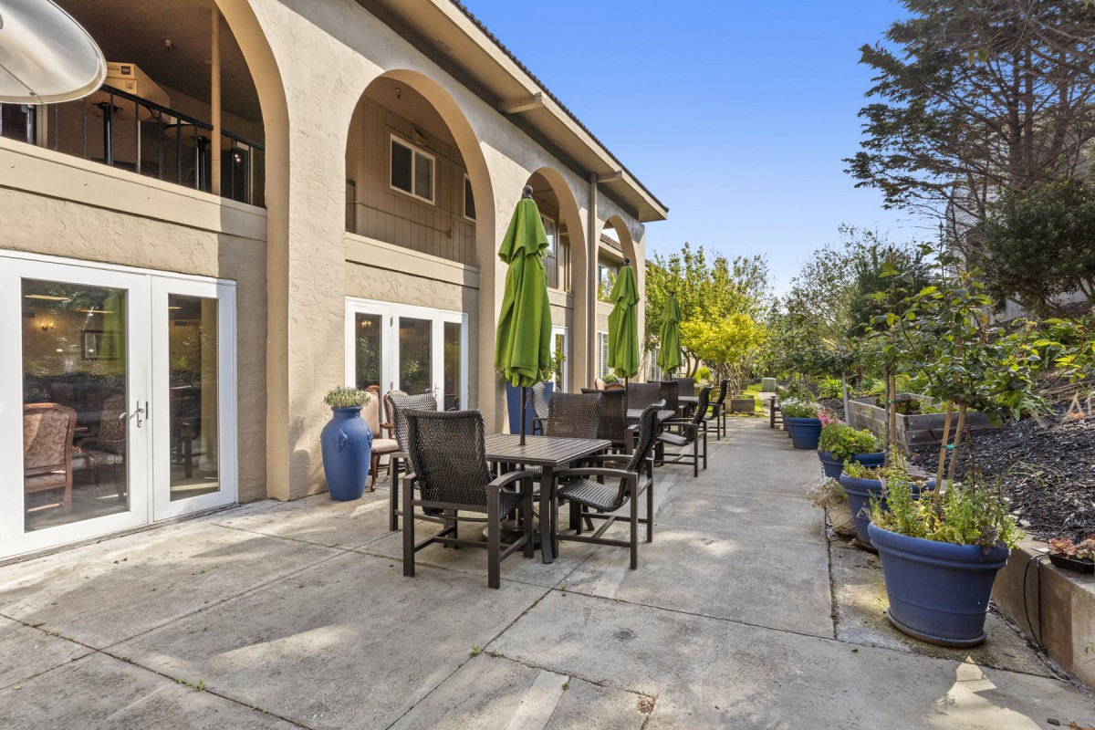 A spacious patio with tables, chairs, and umbrellas outside a building with arched architecture.