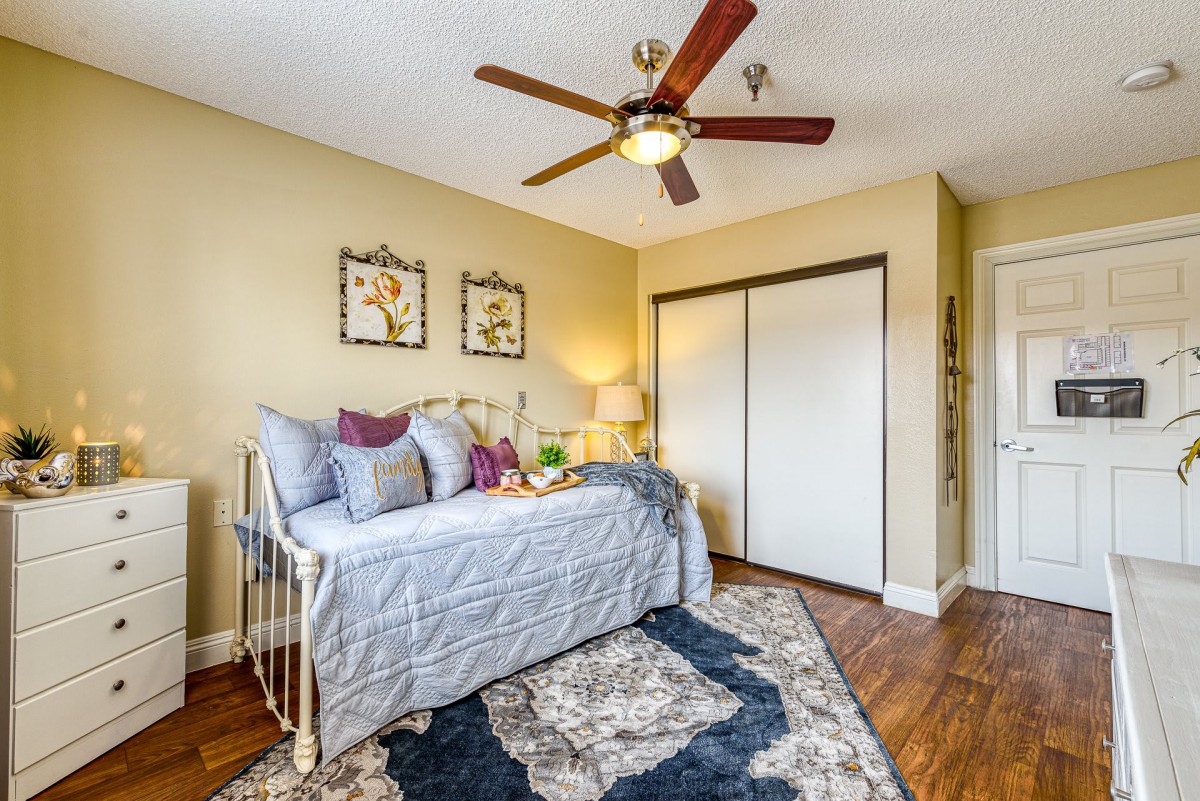 A cozy bedroom with a daybed, featuring a ceiling fan and wooden flooring.