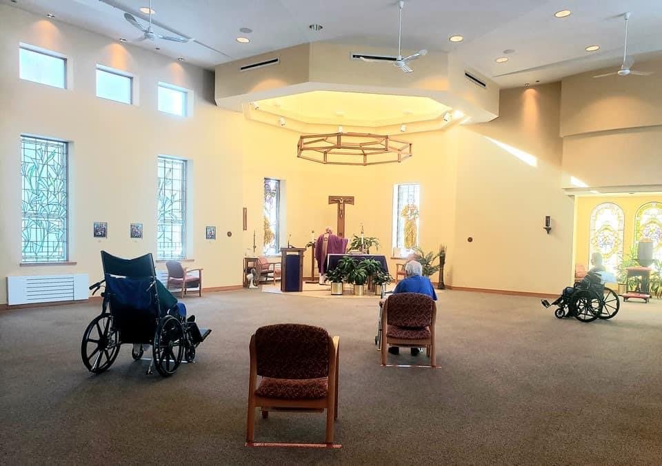 A serene chapel interior with chairs and wheelchairs arranged facing the altar.