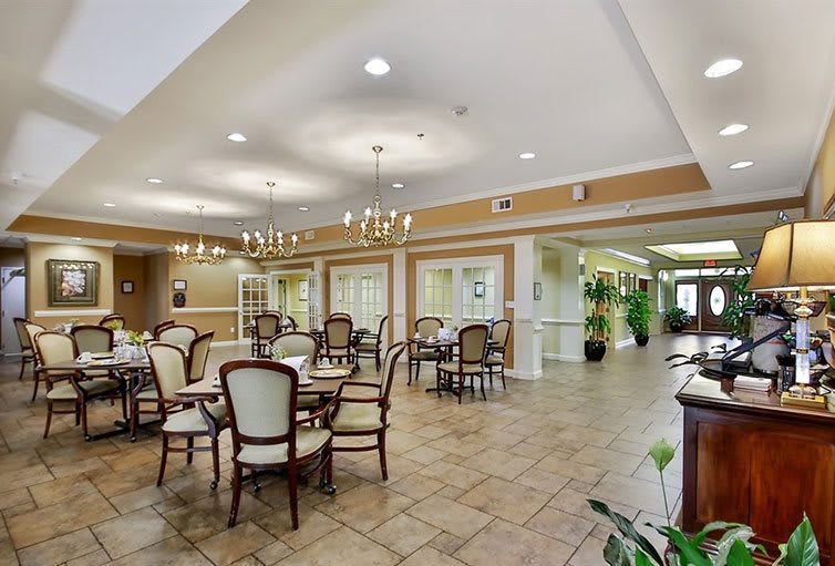A well-lit dining area with multiple tables and chairs, featuring chandeliers and elegant decor.