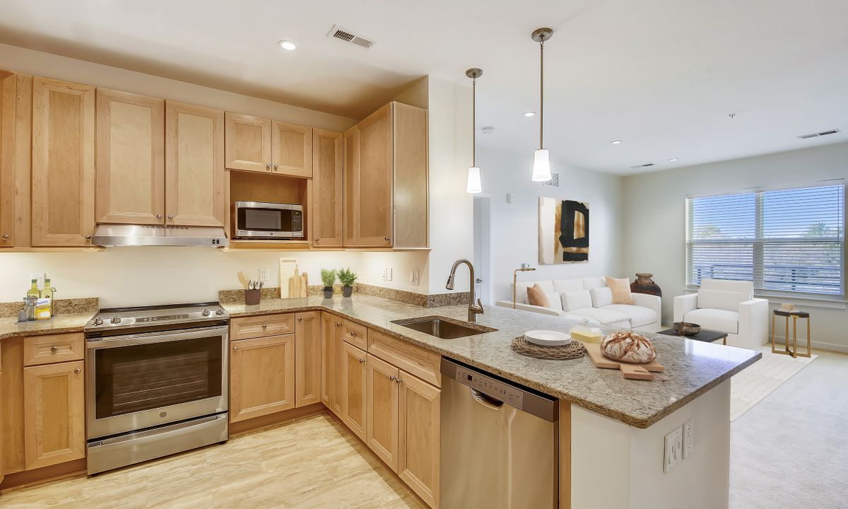 A modern kitchen with wood cabinets and stainless steel appliances in an open floor plan.