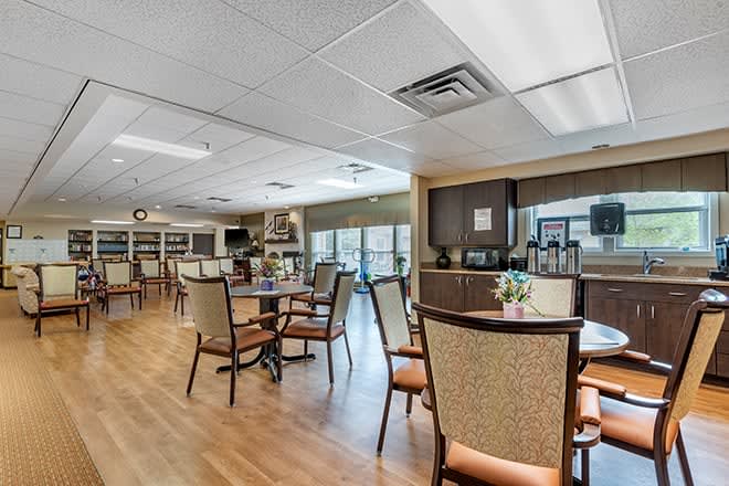 A spacious dining area with tables and chairs, featuring a wooden floor and ample natural light.