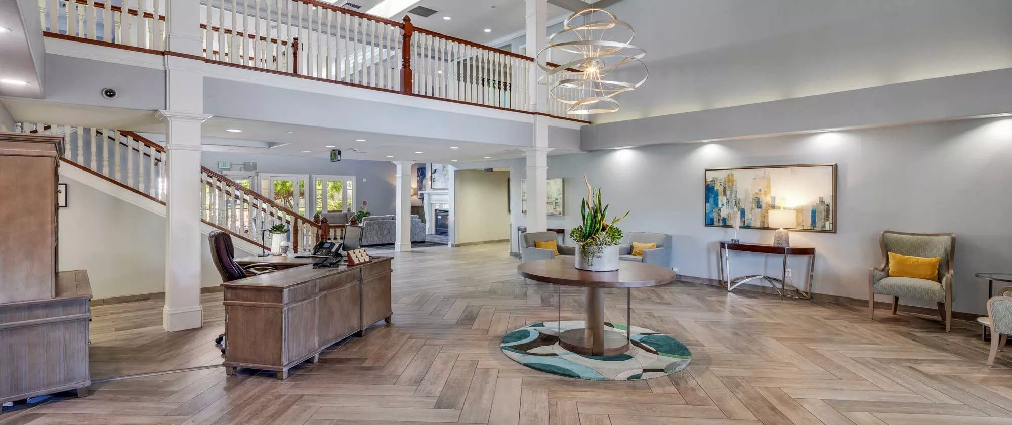 A spacious and modern lobby with elegant furnishings, featuring a large chandelier and wooden flooring.