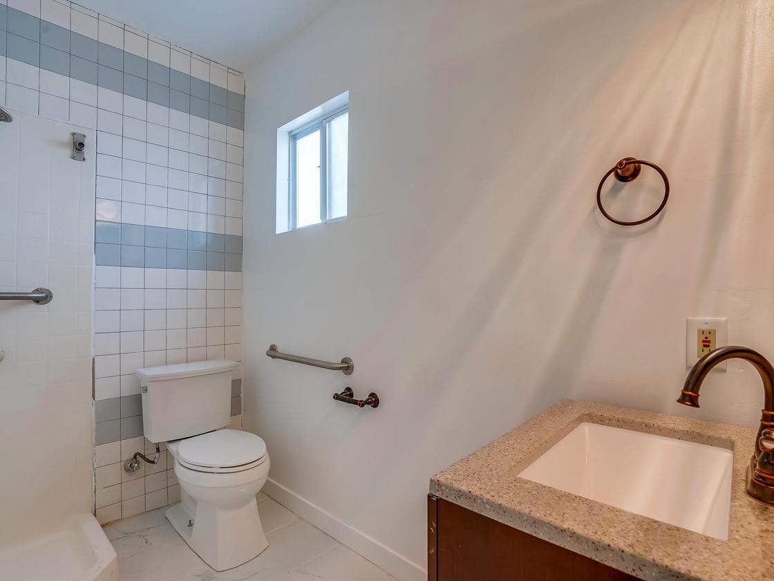 A modern bathroom with a tiled wall, featuring a toilet, sink, and a small window.