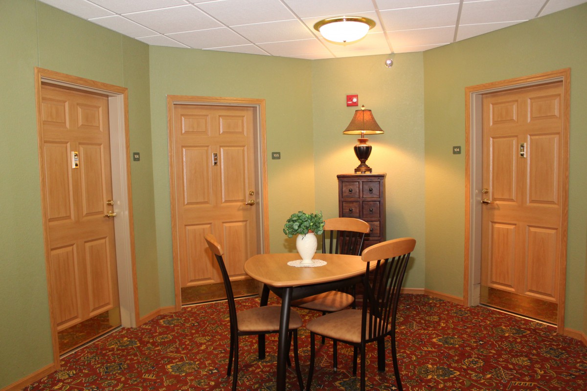 A cozy interior space with a table and chairs, surrounded by doors, featuring a lamp on a side cabinet.