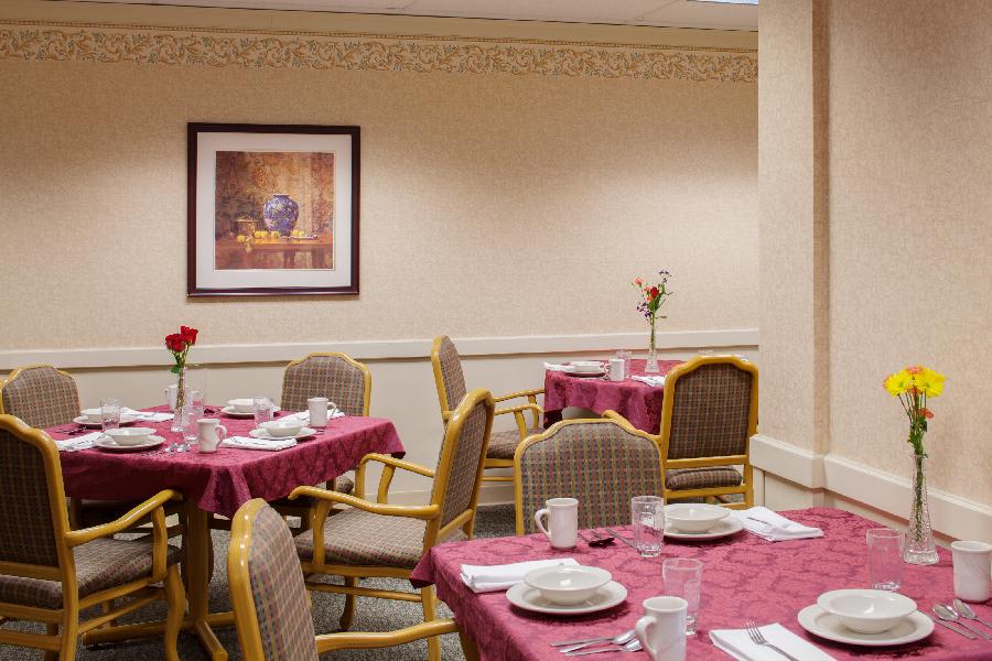 A neatly arranged dining area with tables covered in red tablecloths, set with white dishware and surrounded by cushioned chairs.