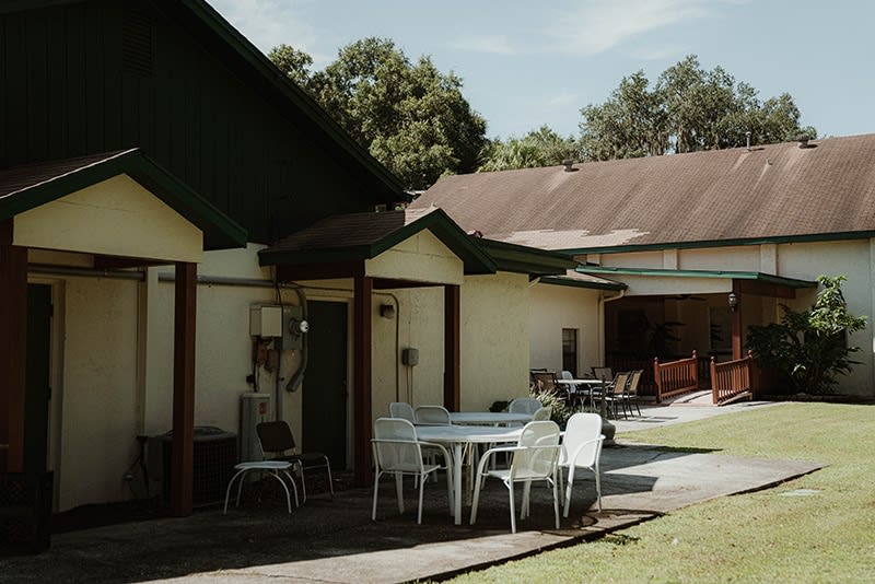 A sunny outdoor patio area with tables and chairs beside a building.