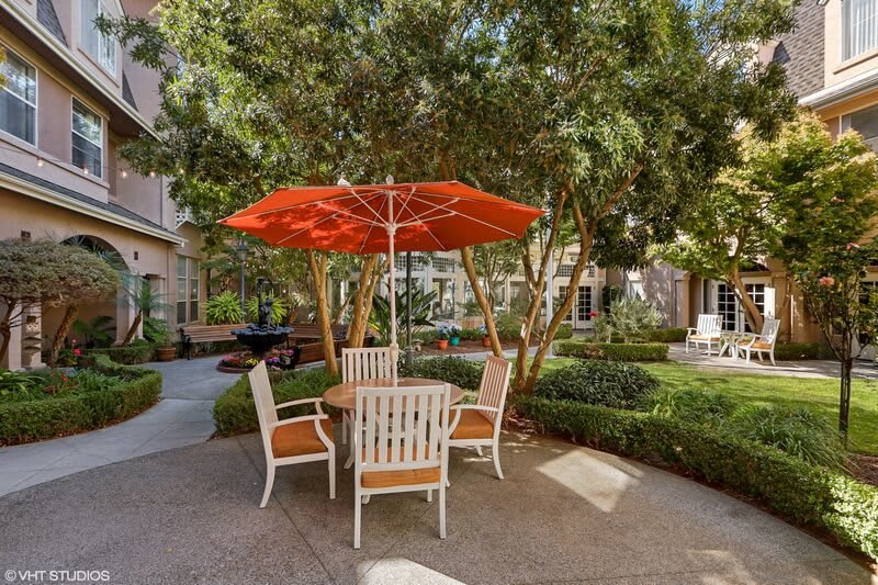 A peaceful outdoor seating area with a red umbrella and patio furniture surrounded by greenery.