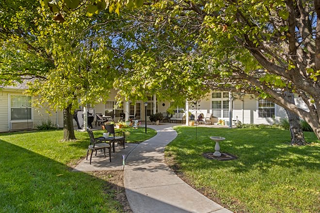 A serene garden area with a winding pathway, outdoor seating, and lush green trees.