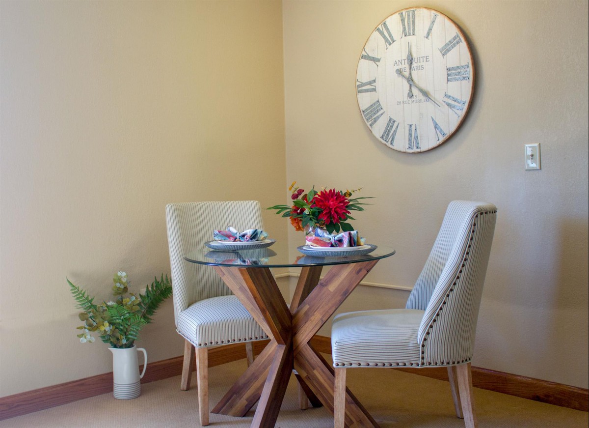 Cozy dining nook with a round table, elegant chairs, and a decorative wall clock.