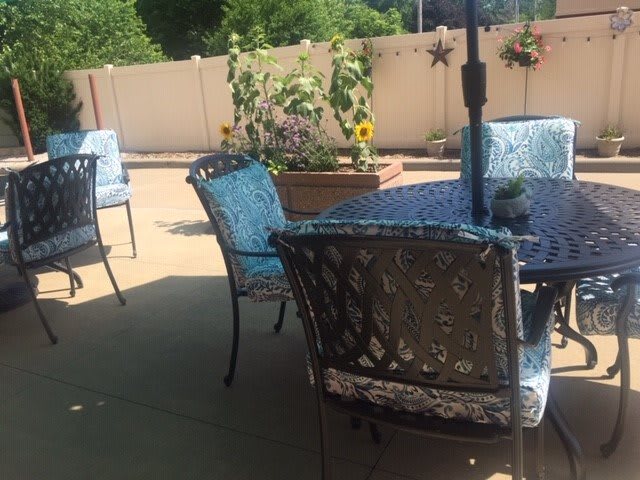 A sunny patio with chairs and a table surrounded by greenery.