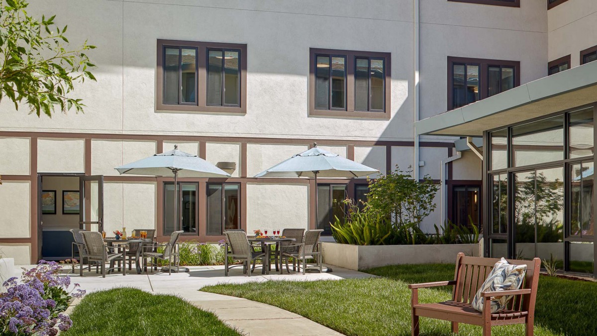 A serene outdoor patio area with tables, chairs, and umbrellas adjacent to a building.
