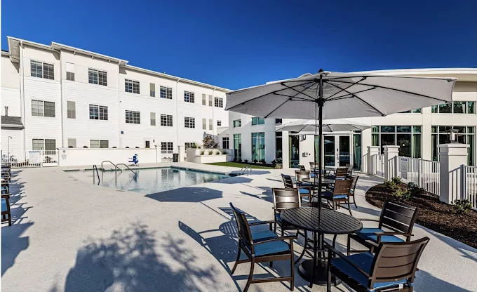 A modern residential complex with a swimming pool and outdoor seating area on a sunny day.