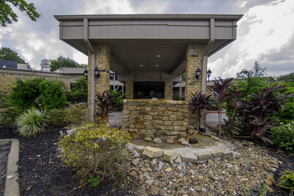 Entrance of a building with stone walls and surrounding greenery.