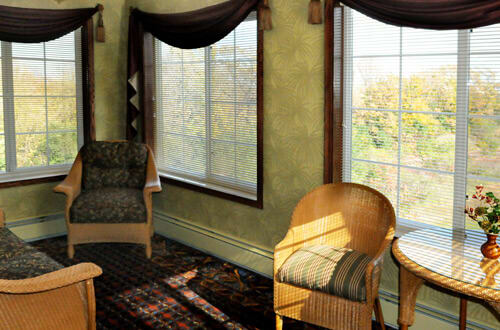 A cozy living room with chairs and large windows letting in sunlight.