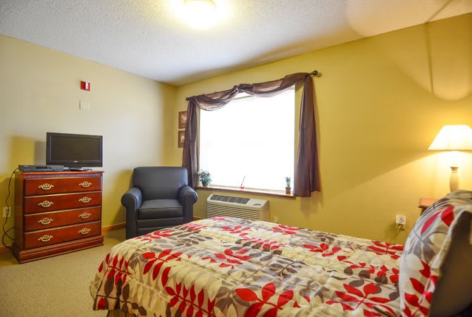 A cozy bedroom with a colorful bedspread, an armchair, and a television.