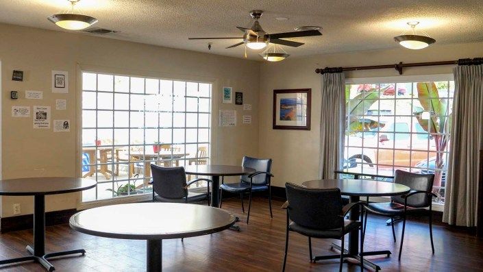 A cozy indoor seating area with round tables, chairs, large windows, and wall art.