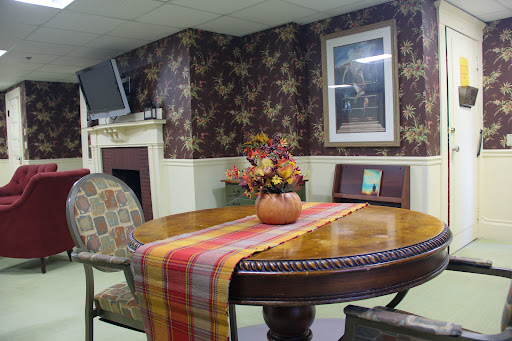 A cozy dining area featuring a wooden table with a colorful table runner and floral arrangement, set against patterned wallpaper.