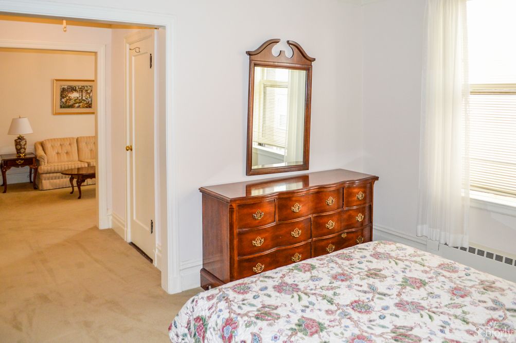 A bedroom featuring a wooden dresser with an attached mirror, next to a bed with floral bedding.