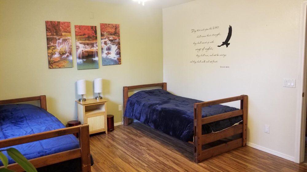 A cozy and minimalist bedroom with a single wooden bed, wall art depicting nature scenes, and a small bedside table.