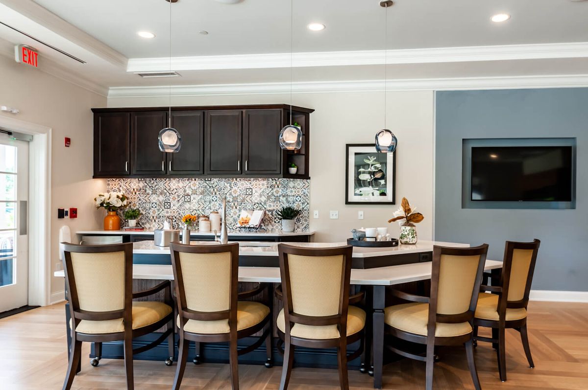 A modern kitchen interior featuring a row of bar stools at the countertop, pendant lighting, and stylish cabinetry.