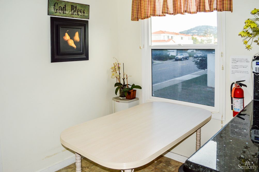 A cozy kitchen corner with a table, plant, and wall art by the window.
