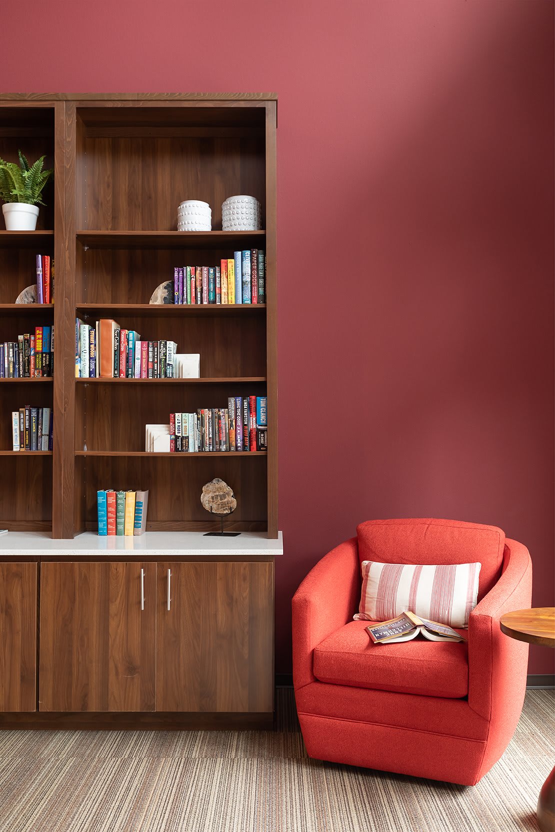 A cozy reading nook featuring a wooden bookshelf filled with books and a comfortable red chair.