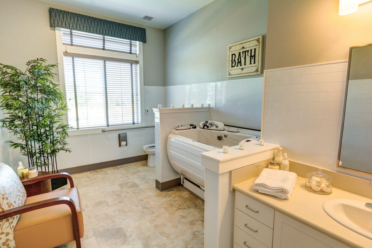 A well-lit bathroom featuring a large bathtub, towels neatly arranged on the counter, and a window providing natural light.